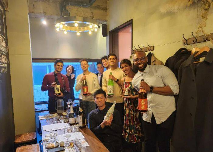 Guests smile and hold big bottles of sake at a sake-tasting experience in Tsukiji.